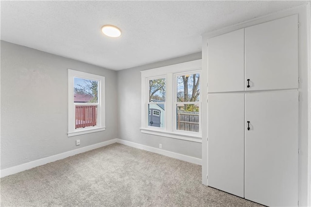 unfurnished bedroom featuring a textured ceiling, light carpet, and multiple windows