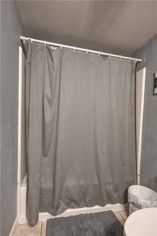 bathroom featuring shower / tub combo, a textured ceiling, and toilet