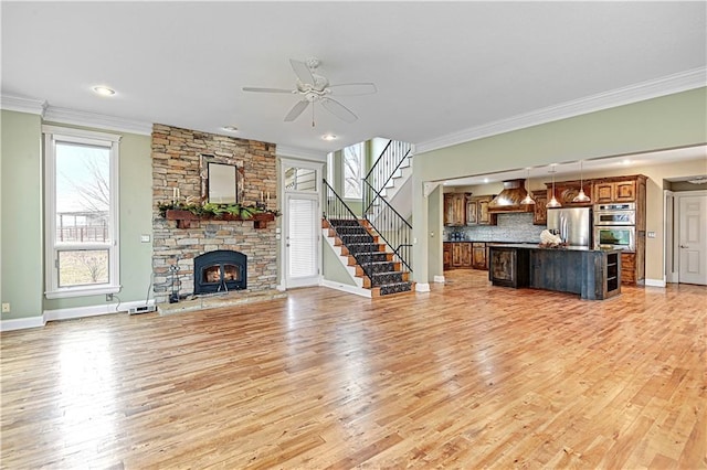 unfurnished living room featuring crown molding, a fireplace, light hardwood / wood-style floors, and ceiling fan