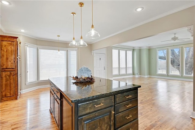 kitchen featuring crown molding, decorative light fixtures, a center island, dark stone counters, and light hardwood / wood-style floors