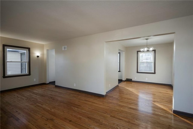 empty room with dark hardwood / wood-style floors and a notable chandelier