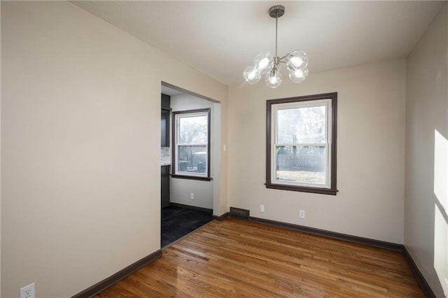 spare room featuring plenty of natural light, hardwood / wood-style floors, and an inviting chandelier