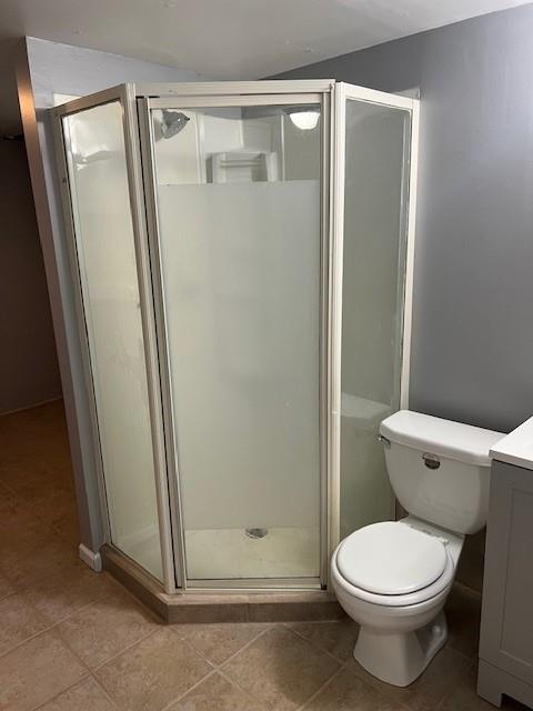 bathroom featuring toilet, vanity, tile patterned floors, and a shower with door