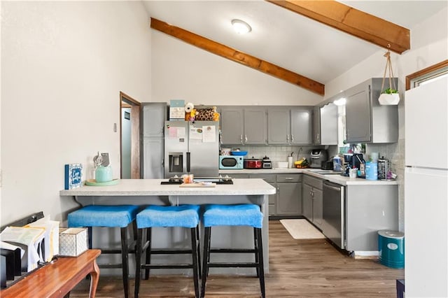 kitchen featuring a breakfast bar area, gray cabinetry, beamed ceiling, stainless steel appliances, and backsplash