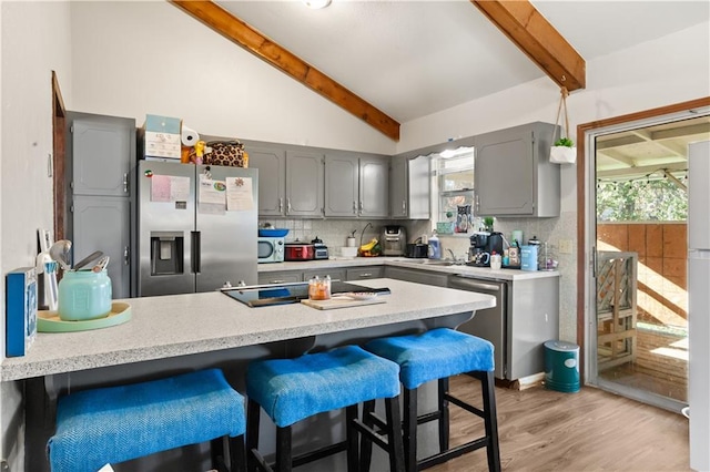 kitchen featuring backsplash, vaulted ceiling with beams, stainless steel appliances, and gray cabinetry