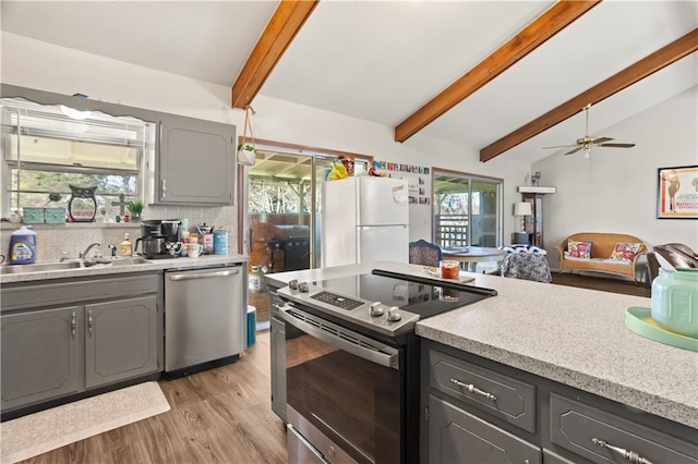 kitchen with sink, gray cabinetry, stainless steel appliances, tasteful backsplash, and lofted ceiling with beams