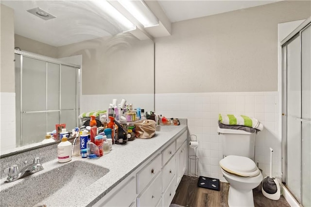 bathroom with wood-type flooring, tile walls, vanity, an enclosed shower, and toilet