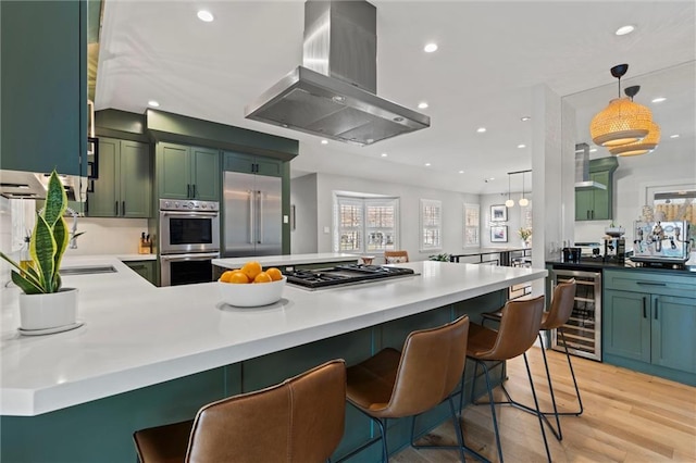 kitchen featuring wine cooler, a breakfast bar, island range hood, appliances with stainless steel finishes, and pendant lighting