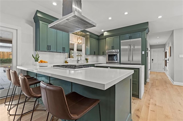 kitchen with a breakfast bar, stainless steel appliances, island range hood, green cabinetry, and kitchen peninsula