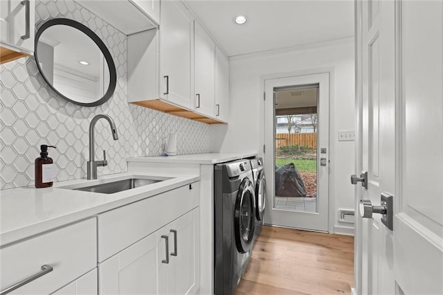 clothes washing area with cabinets, sink, washer and clothes dryer, and light hardwood / wood-style floors