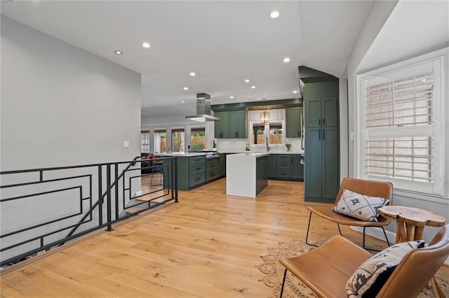 interior space featuring green cabinets, a center island, island range hood, stainless steel gas cooktop, and light wood-type flooring