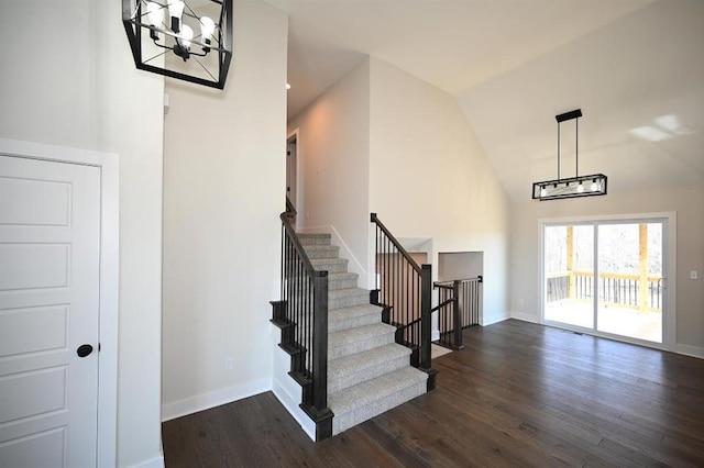 stairs featuring lofted ceiling, wood-type flooring, and an inviting chandelier