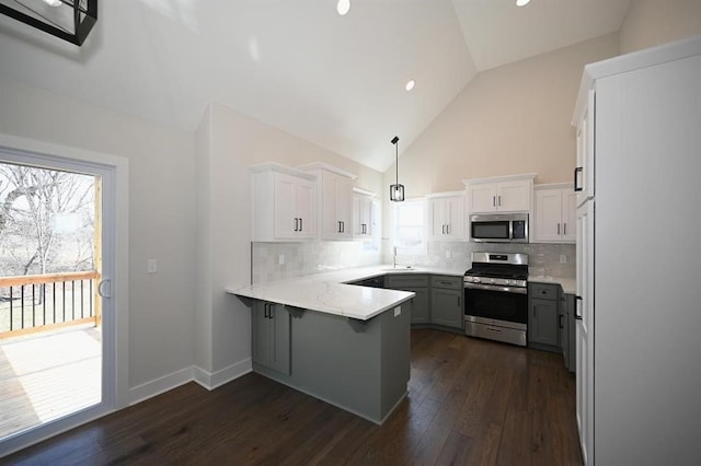 kitchen with kitchen peninsula, appliances with stainless steel finishes, dark wood-type flooring, pendant lighting, and white cabinetry