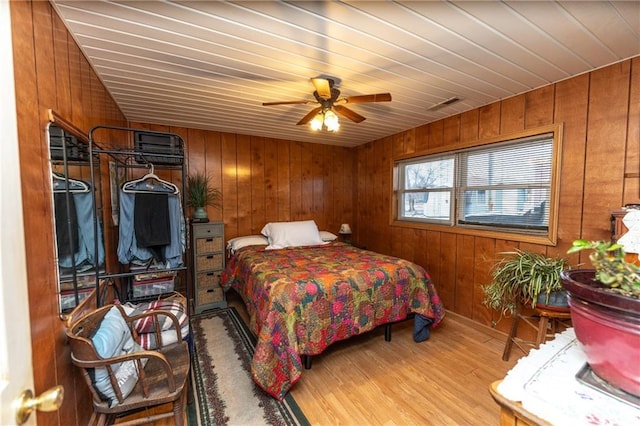 bedroom with ceiling fan, hardwood / wood-style floors, and wooden walls