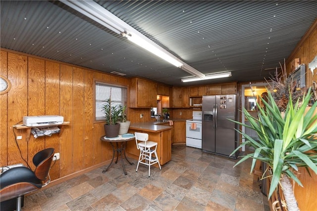 kitchen with white electric range oven, a kitchen breakfast bar, stainless steel refrigerator with ice dispenser, kitchen peninsula, and wooden walls