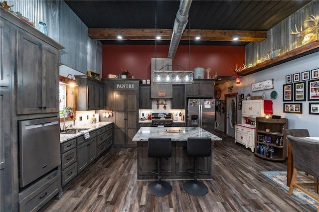 kitchen with a center island, a high ceiling, sink, appliances with stainless steel finishes, and beamed ceiling