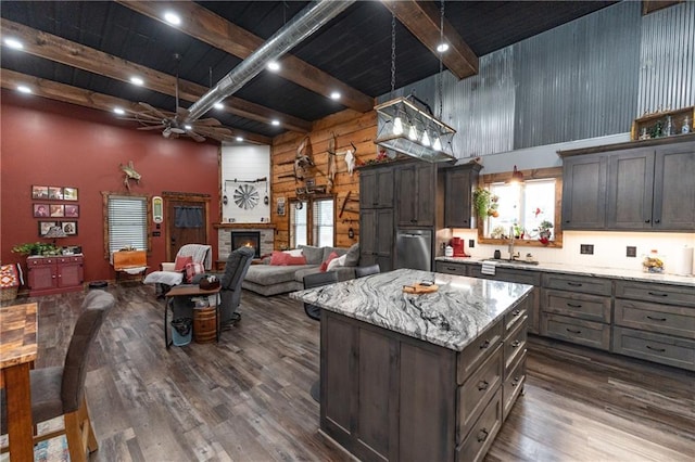 kitchen featuring a center island, a stone fireplace, hanging light fixtures, dark hardwood / wood-style floors, and beam ceiling