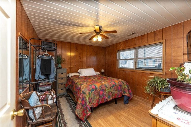 bedroom with ceiling fan, wood-type flooring, and wooden walls