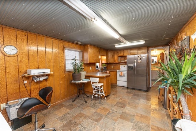 kitchen with stainless steel fridge with ice dispenser, wooden walls, white range with electric cooktop, and a breakfast bar area