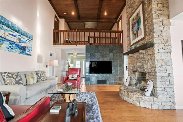 living room with wood-type flooring, a towering ceiling, a stone fireplace, and wooden ceiling