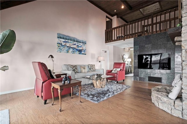 living room featuring hardwood / wood-style floors, a towering ceiling, a stone fireplace, and wooden ceiling