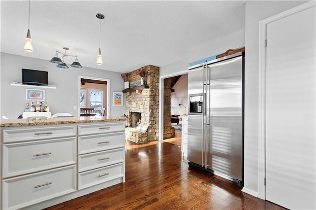 kitchen with stainless steel built in refrigerator, dark wood-type flooring, pendant lighting, a fireplace, and white cabinetry