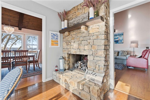 living room with beamed ceiling, a notable chandelier, a stone fireplace, and wood-type flooring