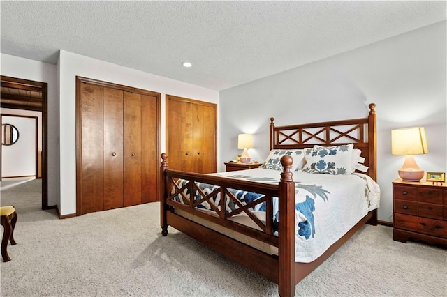 bedroom with light carpet, a textured ceiling, and two closets