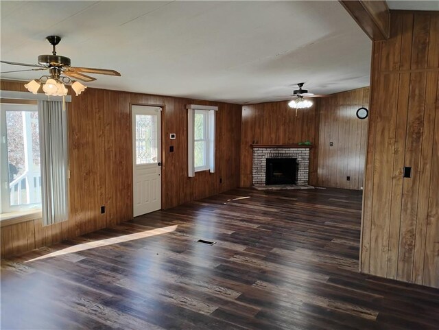 unfurnished living room featuring wood walls, dark hardwood / wood-style flooring, ceiling fan, and a brick fireplace