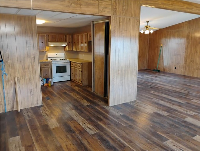 kitchen with gas range gas stove, dark wood-type flooring, and wood walls