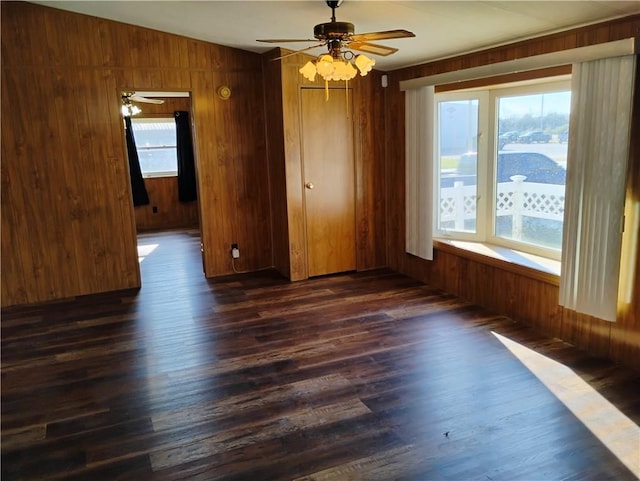 empty room featuring ceiling fan, a wealth of natural light, dark wood-type flooring, and wood walls