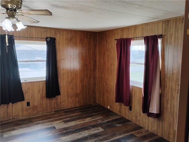 unfurnished room with a textured ceiling, ceiling fan, wood walls, and dark wood-type flooring