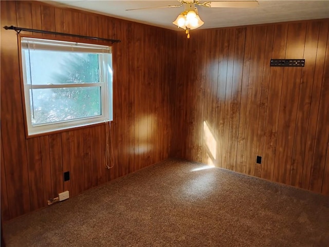 unfurnished room featuring carpet flooring, wood walls, and ceiling fan