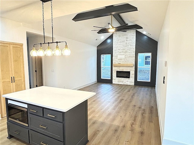 kitchen featuring ceiling fan, stainless steel microwave, lofted ceiling with beams, decorative light fixtures, and a kitchen island