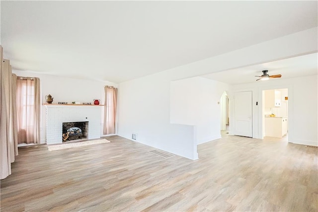 unfurnished living room with a brick fireplace, ceiling fan, and light wood-type flooring