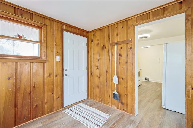 entryway with light wood-type flooring and wooden walls