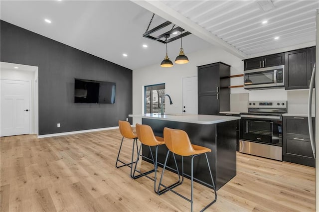 kitchen with sink, a kitchen bar, an island with sink, pendant lighting, and appliances with stainless steel finishes