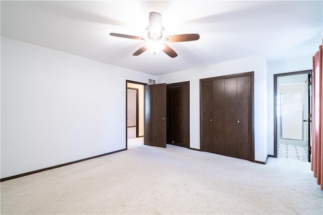 unfurnished bedroom with ceiling fan, light colored carpet, and two closets