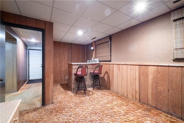 bar featuring light carpet, a paneled ceiling, and wooden walls