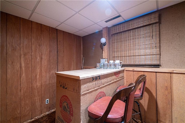 bar with tile counters, a drop ceiling, and wood walls