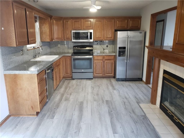 kitchen featuring decorative backsplash, stainless steel appliances, sink, light hardwood / wood-style floors, and a tiled fireplace