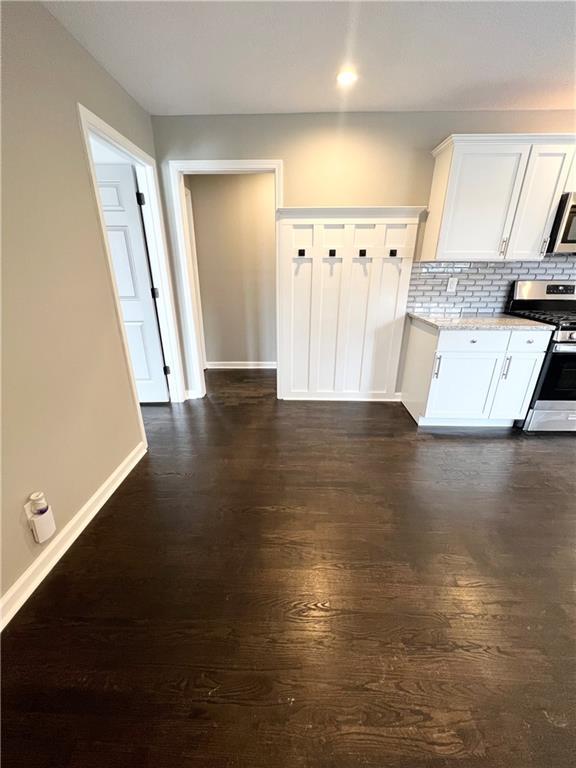 kitchen featuring white cabinetry, light stone countertops, dark hardwood / wood-style floors, backsplash, and appliances with stainless steel finishes