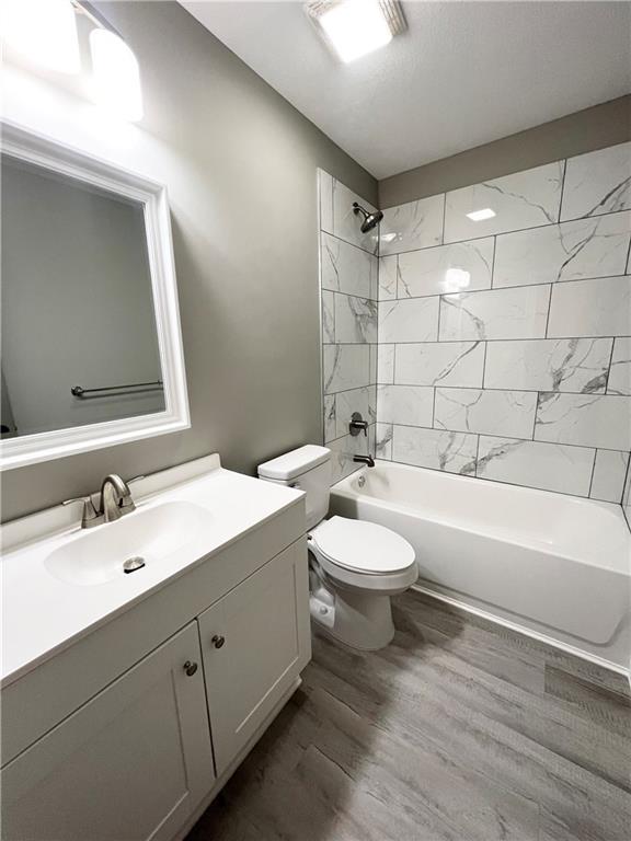 full bathroom featuring tiled shower / bath combo, toilet, wood-type flooring, and vanity