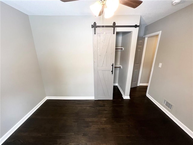 unfurnished bedroom with ceiling fan, a barn door, dark wood-type flooring, and a closet