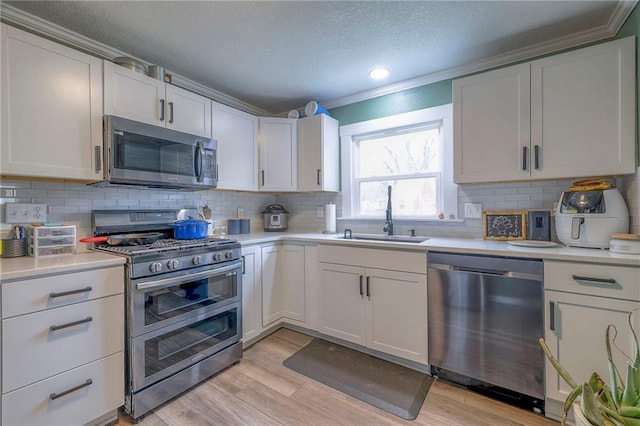 kitchen with sink, light hardwood / wood-style flooring, ornamental molding, appliances with stainless steel finishes, and white cabinetry