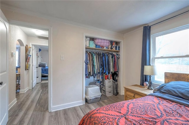 bedroom with multiple windows, wood-type flooring, a closet, and ornamental molding