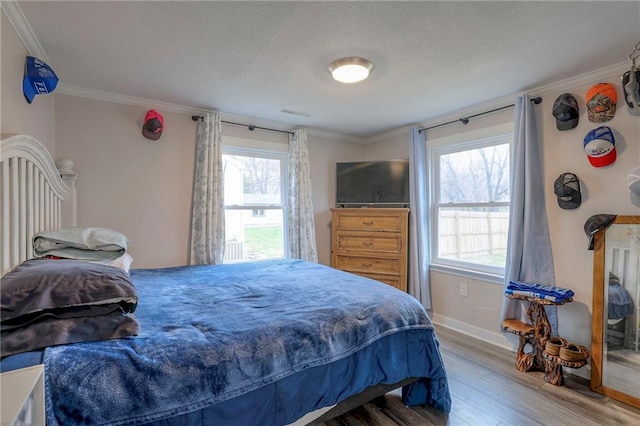 bedroom featuring multiple windows, wood-type flooring, a textured ceiling, and ornamental molding