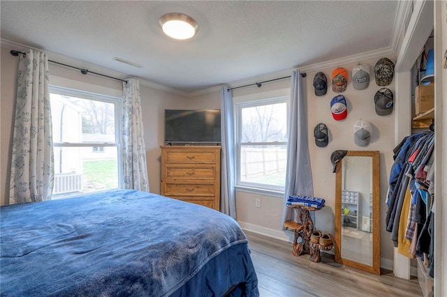 bedroom featuring hardwood / wood-style floors, a textured ceiling, multiple windows, and crown molding