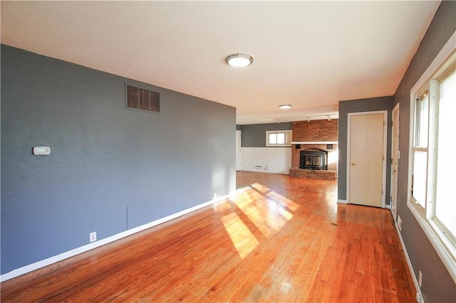 unfurnished living room with wood-type flooring and a brick fireplace