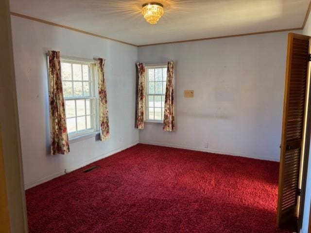 carpeted empty room with plenty of natural light, an inviting chandelier, and ornamental molding